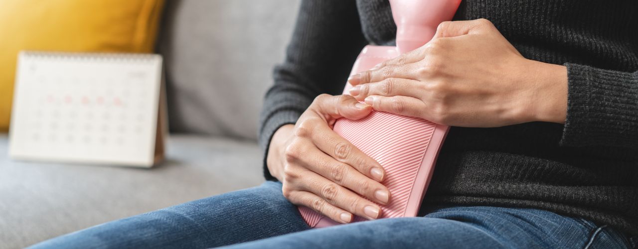 Frau, die unter Menstruationsbeschwerden leidet, mit Heißwasserbeutel